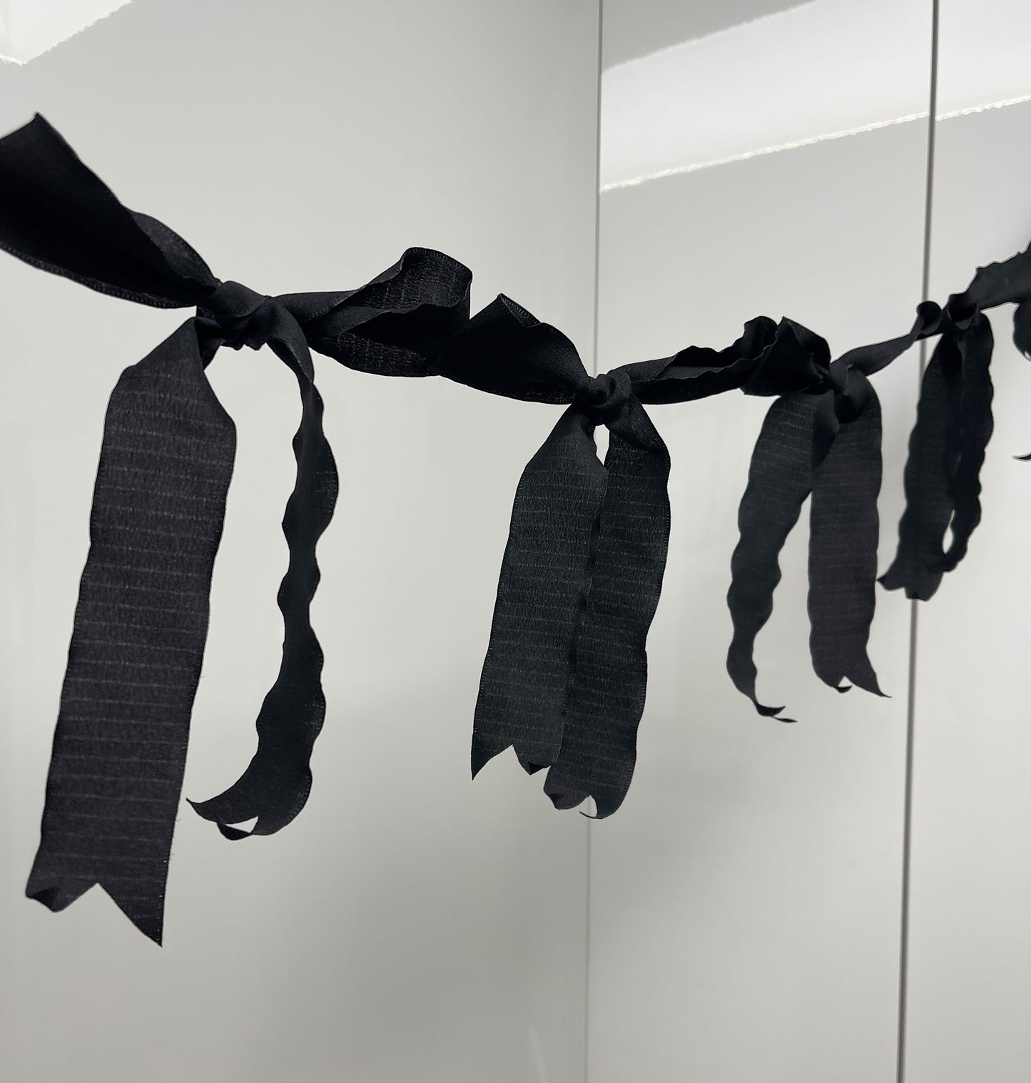 Black Ribbon Bow Garland Hanging against white background. 10 Bows per garland.
